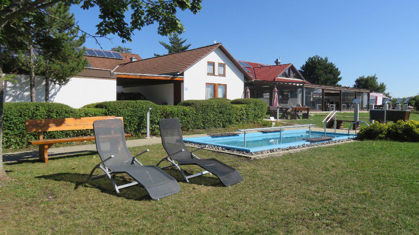 Zwei Liegen am Wassertretbecken, im Hintergrund die Gaststätte "Öfinger Landhaus"